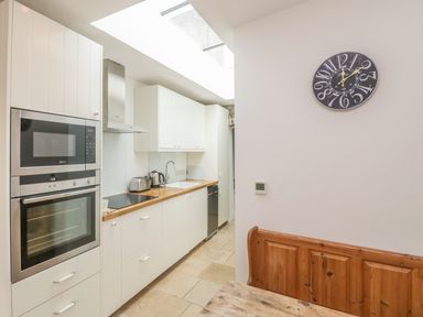 A kitchen with white cabinets a wooden countertop built in oven microwave toaster kettle and a wall clock at Apple Tree Cottage in Shillingstone near Sturminster Newton