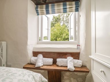 A wooden bench with folded white towels under a window with blue and white striped curtain and a view of trees at Apple Tree Cottage in Shillingstone near Sturminster Newton