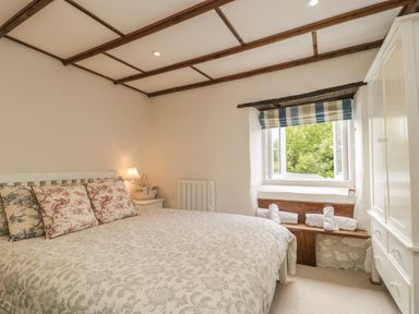 A bedroom with a bed pillows a nightstand lamp a window with a striped blind and a white wardrobe at Apple Tree Cottage in Shillingstone near Sturminster Newton