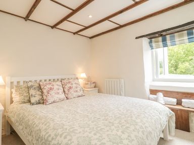 A bedroom with a bed with patterned pillows and blankets bedside tables lamps and a window with rolled towels at Apple Tree Cottage in Shillingstone near Sturminster Newton