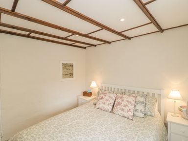 A bedroom with a double bed, patterned bedding, two bedside tables with lamps and a framed picture on the wall at Apple Tree Cottage in Shillingstone near Sturminster Newton