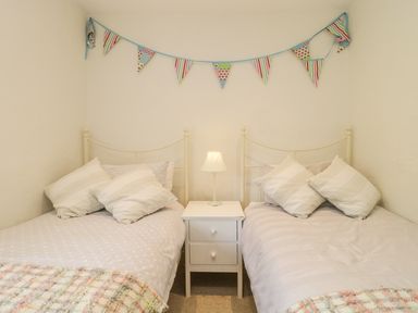 A bedroom with two single beds separated by a white nightstand with a lamp and bunting on the wall at Apple Tree Cottage in Shillingstone near Sturminster Newton