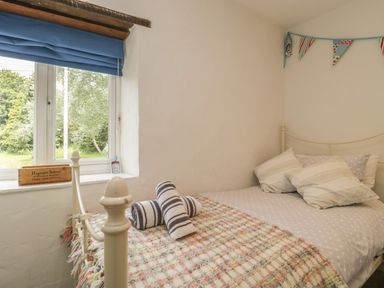 A bedroom with a metal bed frame pillows rolled towels and a window with a blue blind at Apple Tree Cottage Shillingstone near Sturminster Newton