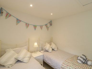 A bedroom with two single beds a white nightstand with a lamp and bunting on the wall at Apple Tree Cottage in Shillingstone near Sturminster Newton