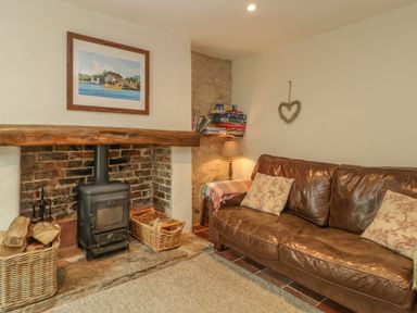 A living room with a wood burner fireplace a leather sofa and a lamp at Apple Tree Cottage in Shillingstone near Sturminster Newton
