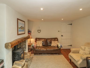 A sitting room with a leather sofa, armchair, wood burning stove, and wooden beam at Apple Tree Cottage in Shillingstone near Sturminster Newton