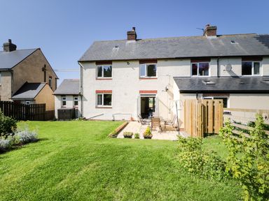 A backyard with a patio table and chairs and a lawn in front of a white two-story house at Bunty's Place in Chatton near Wooler