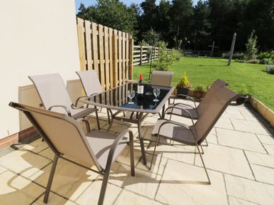 A patio with six chairs arranged around a glass table with a bottle and four glasses on it at Bunty's Place in Chatton near Wooler