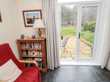 A room with a wooden bookshelf a red chair a lamp and a glass door leading to a patio and garden at Bunty's Place Chatton near Wooler