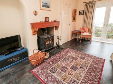 A living room with a wood-burning stove television baskets carpet and a chair at Bunty's Place in Chatton near Wooler