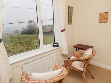 A corner with two wicker chairs with cushions near a window and a small wooden table at Bunty's Place in Chatton near Wooler