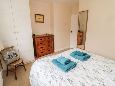 A bedroom with a bed with floral bedding folded towels on the bed a wooden chair with an owl cushion a chest of drawers a white wardrobe and a wall mirror at Bunty's Place in Chatton near Wooler