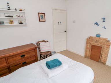 A bedroom with a bed folded towels a wooden chair a chest of drawers and wall shelves with nautical decor at Buntys Place in Chatton near Wooler