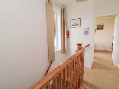 A hallway with a wooden banister and window with curtains at Buntys Place in Chatton near Wooler