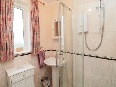 A bathroom with a shower enclosure sink trash bin cabinet window with patterned curtains and a towel at Buntys Place in Chatton near Wooler