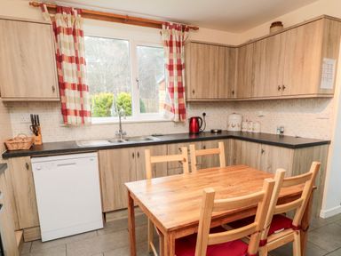 A kitchen with wooden cabinets a dishwasher a table with chairs and a window with checkered curtains at Bunty's Place Chatton near Wooler