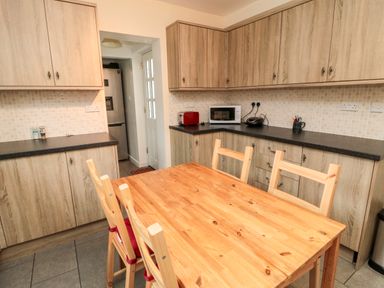 A kitchen with wooden cabinets a wooden dining table and chairs a microwave toaster and refrigerator at Bunty's Place in Chatton near Wooler