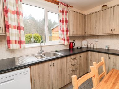 A kitchen with wooden cabinets a double sink a dishwasher a red kettle jars and a wooden table with chairs at Bunty's Place Chatton near Wooler