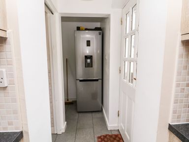 A kitchen hallway with a silver refrigerator a broom and a white door with glass panels at Bunty's Place in Chatton near Wooler