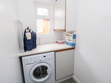 A laundry room with a washing machine a countertop cabinets a window and laundry supplies at Bunty's Place in Chatton near Wooler