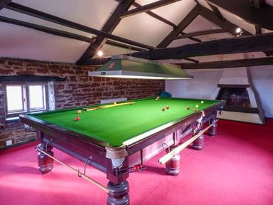 A snooker table with balls and cues in a room with red carpet stone wall and a fireplace at Eden House Edenhall near Penrith