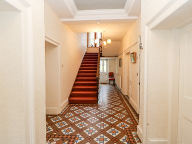 A hallway with patterned tiled floor a red-carpeted staircase a chandelier and a chair near the door at Eden House Edenhall near Penrith
