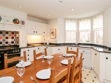 A kitchen with a wooden dining table set with plates and glasses white cabinets and a corner window at Eden House Edenhall near Penrith