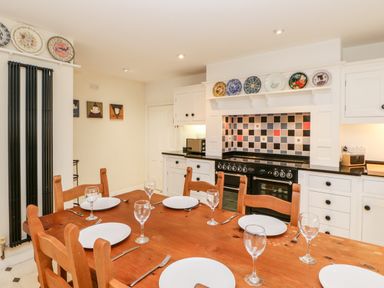 A kitchen with a wooden dining table set with plates and glasses and a stove with decorative plates above Eden House Edenhall near Penrith