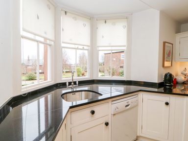 A kitchen corner with black countertops a sink under three windows and white cabinets at Eden House Edenhall near Penrith