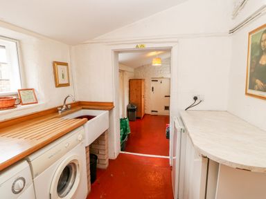 A utility room with a washing machine, sink, countertop, trash bin, and framed pictures at Eden House Edenhall near Penrith