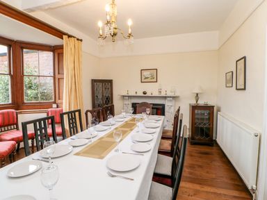 A dining room with a long table set with plates and glasses a chandelier and a fireplace at Eden House Edenhall near Penrith