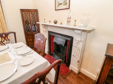 A dining room with a table set with plates and glasses next to a marble fireplace with decorative items on the mantel at Eden House Edenhall near Penrith