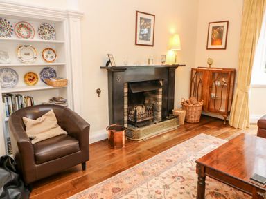 A living room with a leather armchair, fireplace, decorative plates on shelves, and a wooden cabinet at Eden House in Edenhall near Penrith