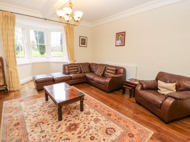 A living room with brown leather sofas a wooden coffee table a patterned rug and windows with beige curtains at Eden House Edenhall near Penrith