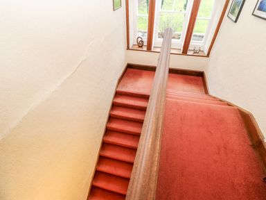 A staircase with red carpet and wooden handrail next to a window with decorative objects at Eden House in Edenhall near Penrith