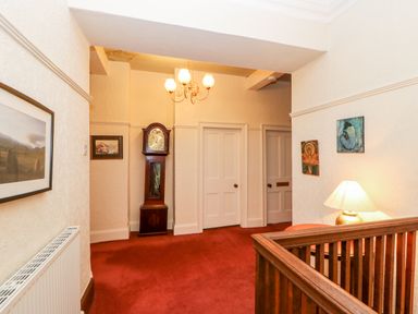 A hallway with red carpet a wooden grandfather clock white doors framed pictures and a lamp on a side table at Eden House Edenhall near Penrith