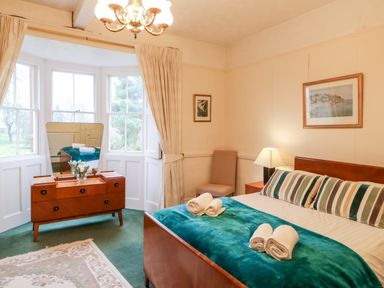 A bedroom with a bed with striped pillows and rolled towels a wooden dresser with a mirror and a chair at Eden House Edenhall near Penrith