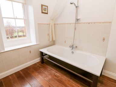 A bathroom with a bathtub a showerhead a window and wooden floorboards at Eden House Edenhall near Penrith