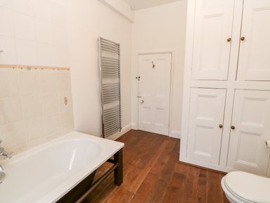A bathroom with a bathtub towel radiator wooden floor built in cupboards and a white door at Eden House Edenhall near Penrith