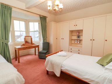 A bedroom with two single beds a wooden dressing table a chair green curtains and built in wardrobes at Eden House Edenhall near Penrith