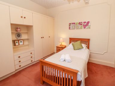 A bedroom with a wooden single bed a bedside table with a lamp built in wardrobes and floral artwork above the bed at Eden House in Edenhall near Penrith