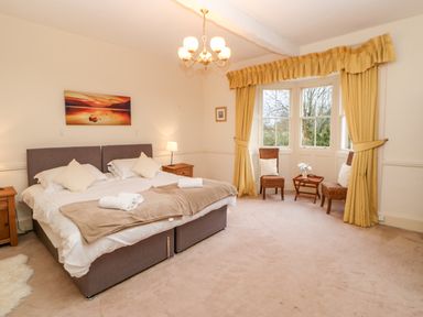 A bedroom with a double bed two wooden bedside tables two chairs and a small table near a window with yellow curtains at Eden House Edenhall near Penrith