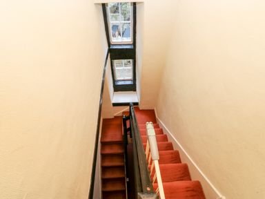 A staircase with red carpet and cream walls next to two windows at Eden House in Edenhall near Penrith