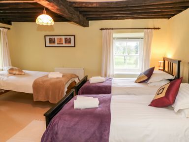 A bedroom with three single beds with folded towels and pillows under a wooden beamed ceiling at Eden House Edenhall near Penrith