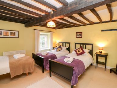 A bedroom with three beds two single beds with purple throws and one bed with a brown throw Eden House Edenhall near Penrith