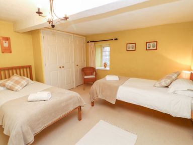 A bedroom with two single beds with beige blankets and plaid pillows a wicker chair and a small window at Eden House Edenhall near Penrith