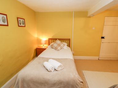 A bedroom with a single bed with pillows and rolled towels a bedside table with a lamp two framed pictures on the wall and a closed door at Eden House Edenhall near Penrith