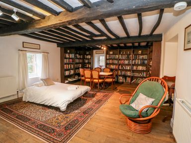 A room with a bed a green cushioned chair a wooden dining table with six chairs and bookshelves lining the wall at Eden House Edenhall near Penrith