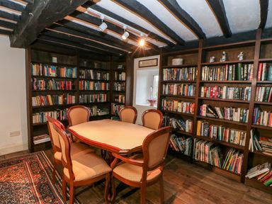 A room with wooden bookshelves filled with books a wooden table with six chairs and exposed ceiling beams at Eden House Edenhall near Penrith