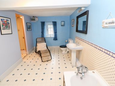 A bathroom with blue walls a bathtub a sink a toilet a wicker chair and a small window with curtains at Eden House Edenhall near Penrith